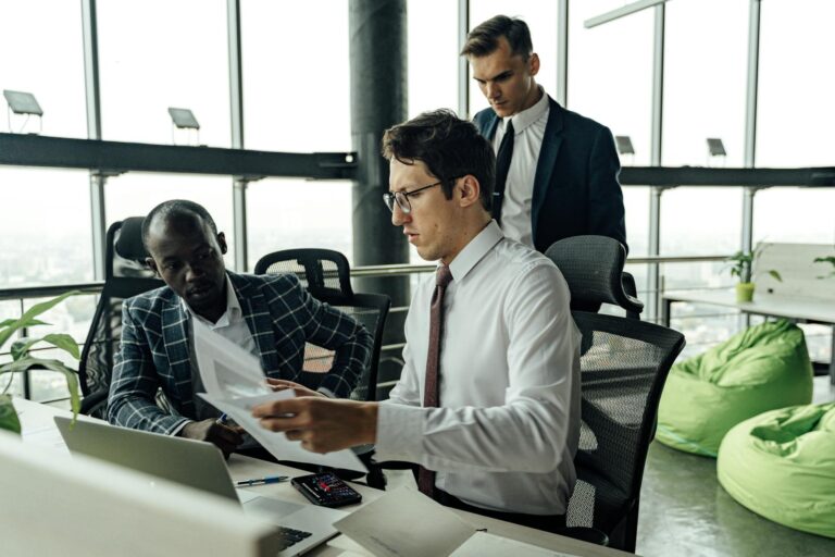 Professionals engaging in teamwork and discussion in a contemporary office setting with large windows.