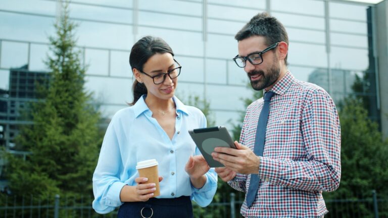 Two professionals discussing work on a tablet outdoors.