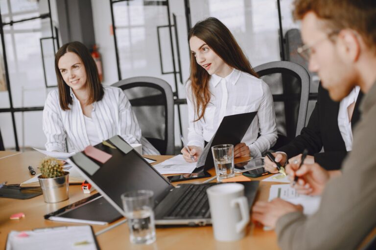 Business team engaged in a collaborative meeting around a table with laptops in a modern office setting.
